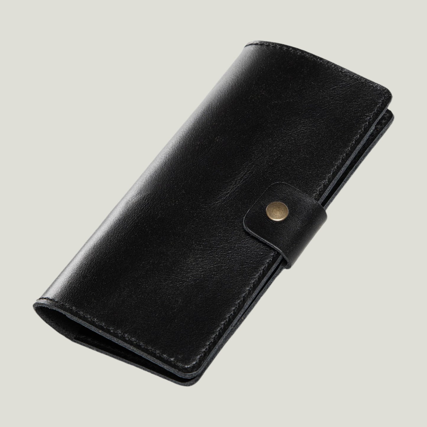 Close-up of the Clark Leather Checkbook Cover in Dexios Black, crafted from top-grain leather with antique brass hardware and a secure snap closure, personalized with fire-branded initials.