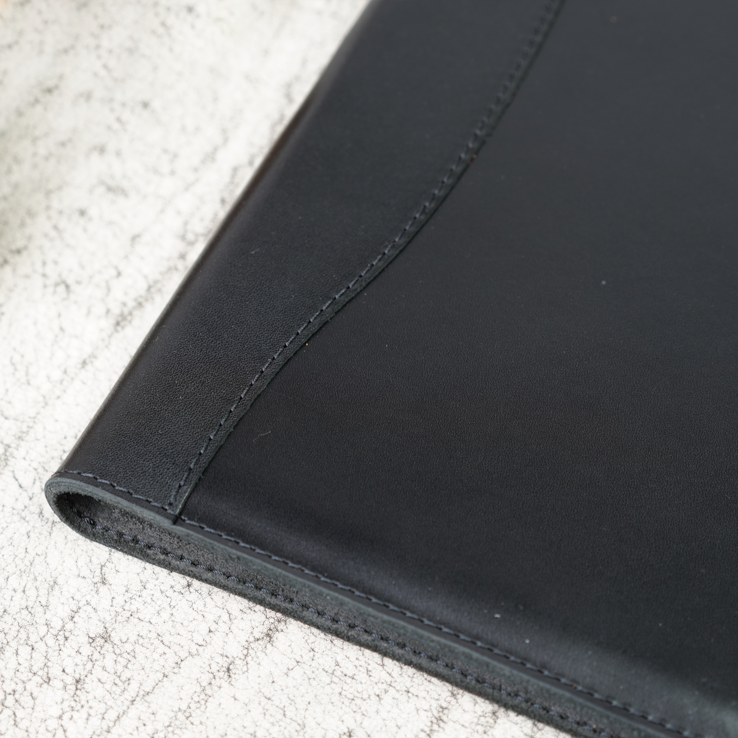 Close-up of the Marshall Padfolio spine and stitching detail in Djor Black leather. Showcases the precise craftsmanship and rich texture of premium full-grain leather.