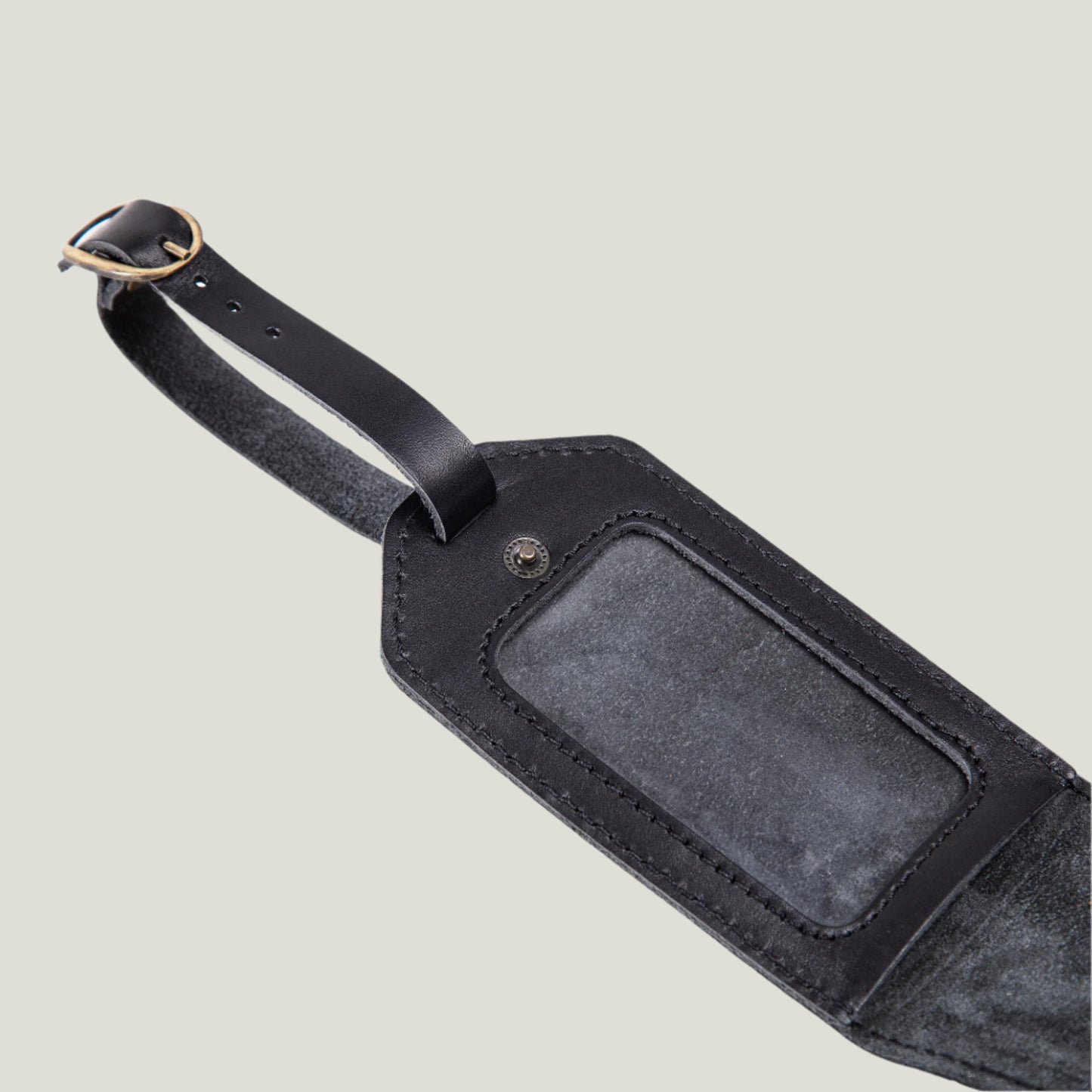 Close-up of a Bond Leather Luggage Tag in Maui Charcoal, featuring suede lining, antique brass hardware, and a personalized fire-branded initial detail.