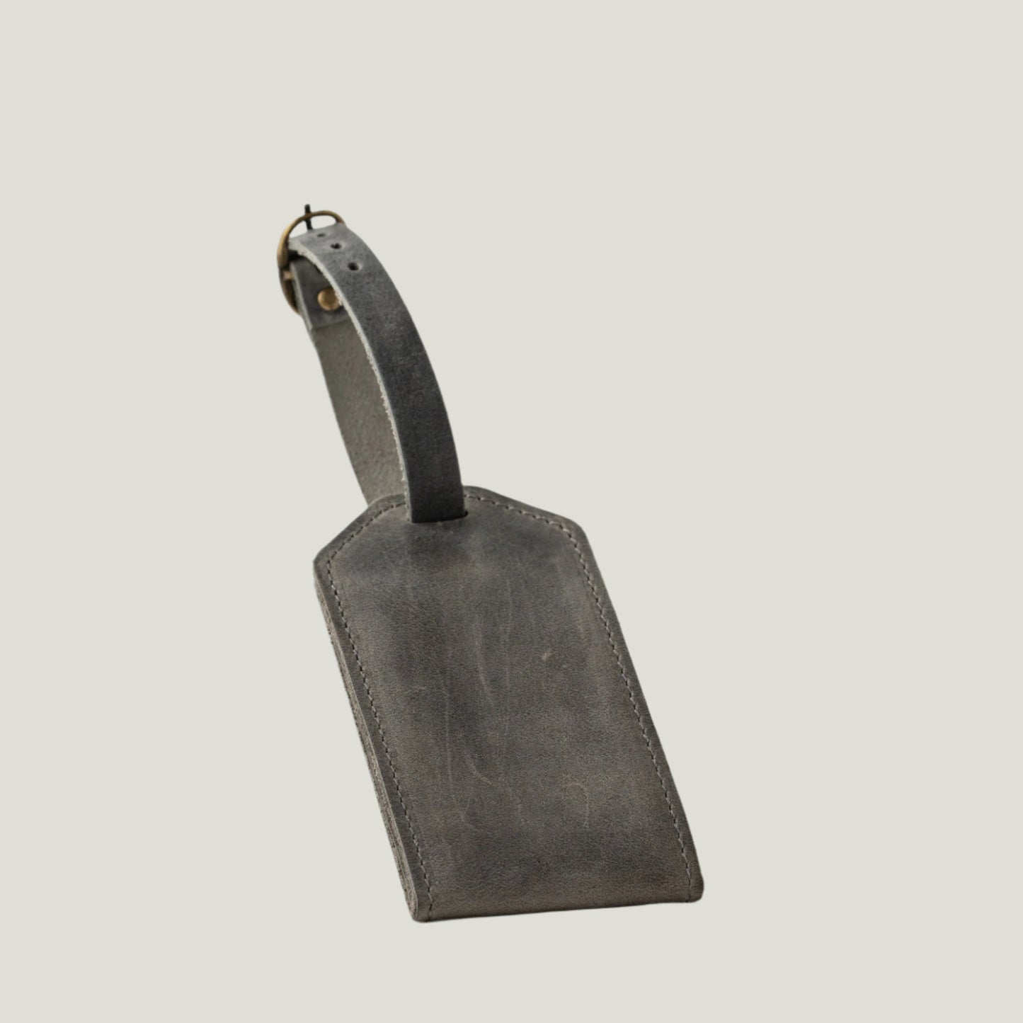 Close-up of the Bond Leather Luggage Tag in Rock, featuring a suede interior, antique brass hardware, and a clear ID sleeve. Personalizable with fire-branded initials.