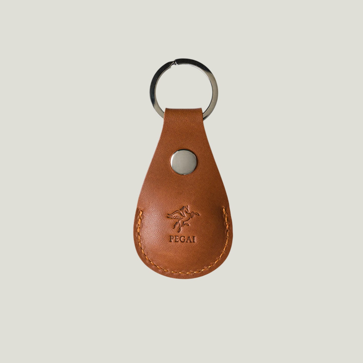 Close-up of Atelier PEGAI’s Pear Leather AirTag Holder in Cognac, crafted in Ubrique, Spain. Sleek design with snap closure and nickel hardware for secure attachment.