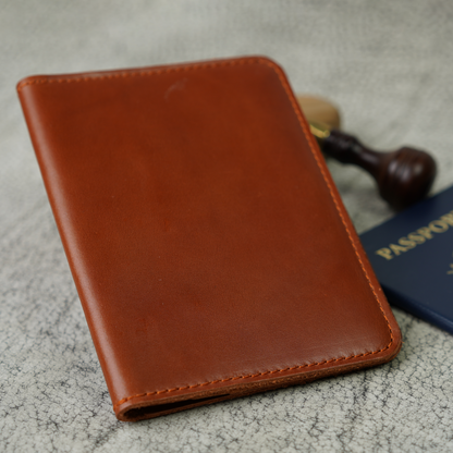 Close-up of the Pike Leather Passport Wallet in rich Dual Tone Whiskey leather, featuring the Atelier PEGAI logo embossed into its warm, full-grain surface. Paired with a passport and wax stamp in the background, this piece celebrates the quiet luxury of true craftsmanship.