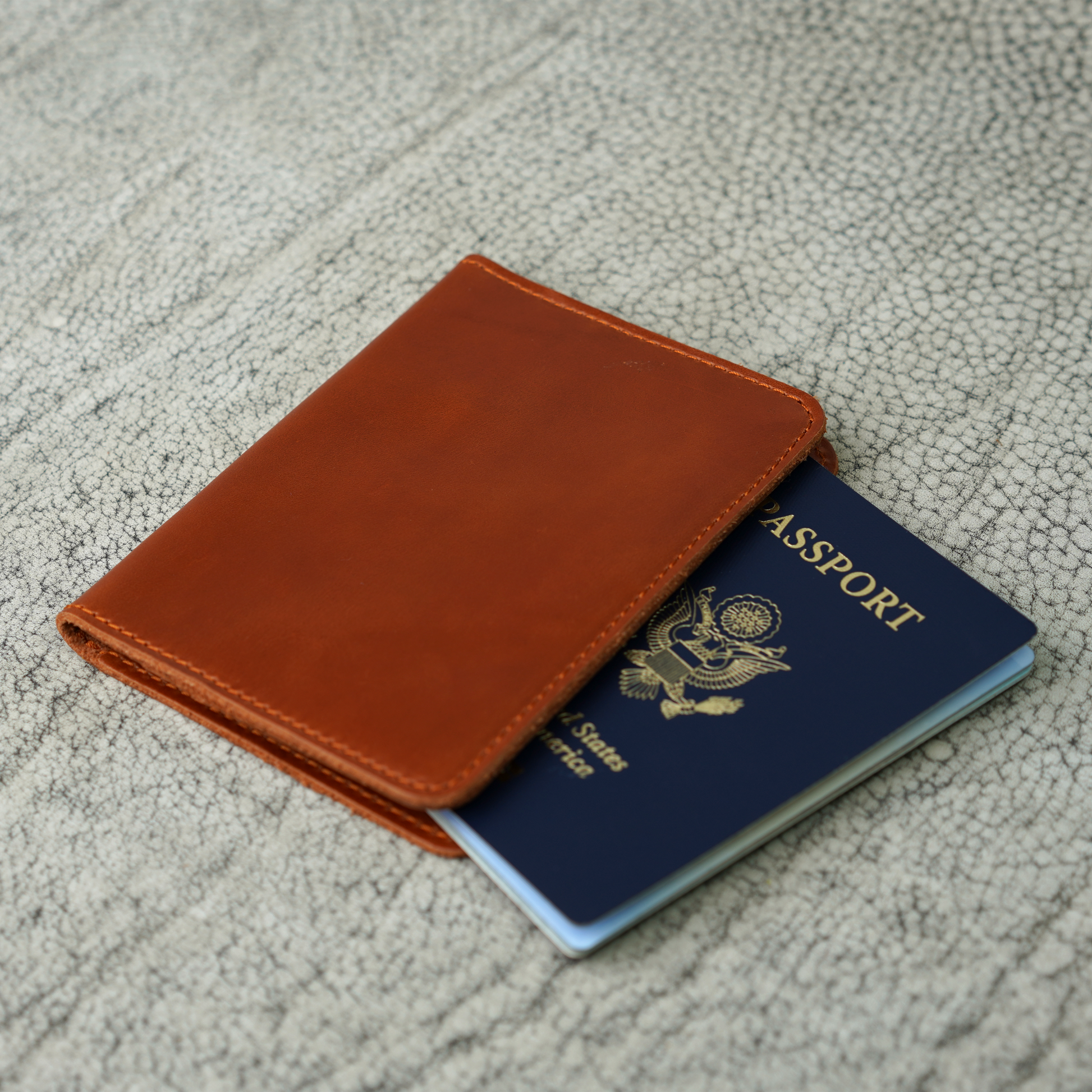 A handcrafted Dual Tone Whiskey leather passport wallet from Atelier PEGAI, partially revealing a U.S. passport. The smooth, golden-brown leather and precise stitching reflect timeless craftsmanship, built for journeys both near and far.