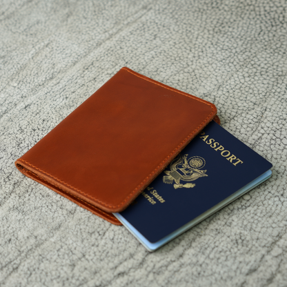 A handcrafted Dual Tone Whiskey leather passport wallet from Atelier PEGAI, partially revealing a U.S. passport. The smooth, golden-brown leather and precise stitching reflect timeless craftsmanship, built for journeys both near and far.