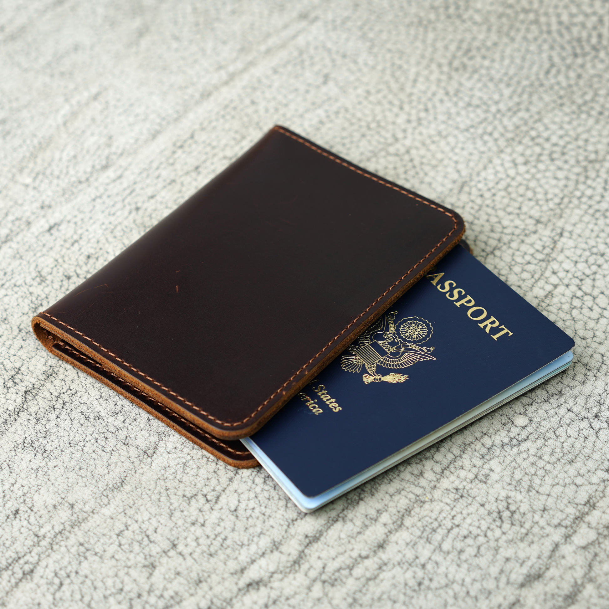 A handcrafted dark brown leather passport wallet partially open to reveal a U.S. passport. The wallet features clean hand-stitched edges, showcasing Atelier PEGAI’s rustic craftsmanship and minimalist design—made to carry stories, not just essentials.
