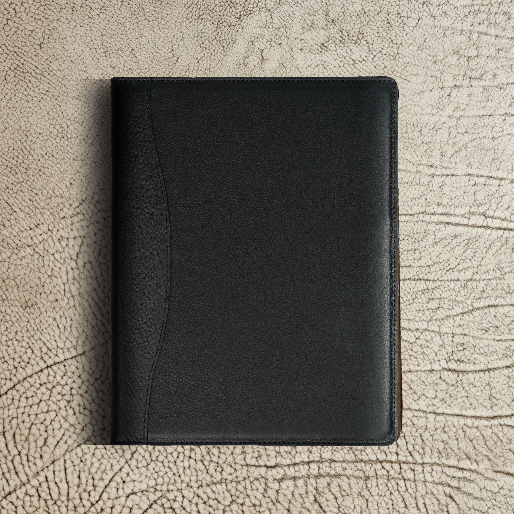 Marshall Leather Legal Padfolio in Dymnos Black shown closed against a textured surface. A minimalist silhouette with premium full-grain leather finish—perfect for those who prefer quiet confidence over clutter.