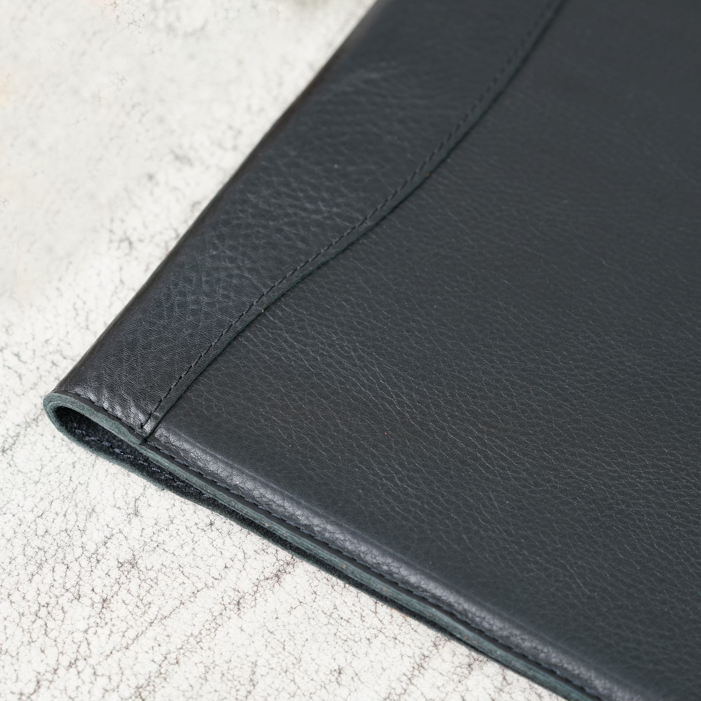 Close-up of the Marshall Padfolio in Dymnos Black, highlighting the rich texture and subtle grain of full-grain leather with tight, hand-stitched detail. A refined blend of craftsmanship and durability from Atelier PEGAI.