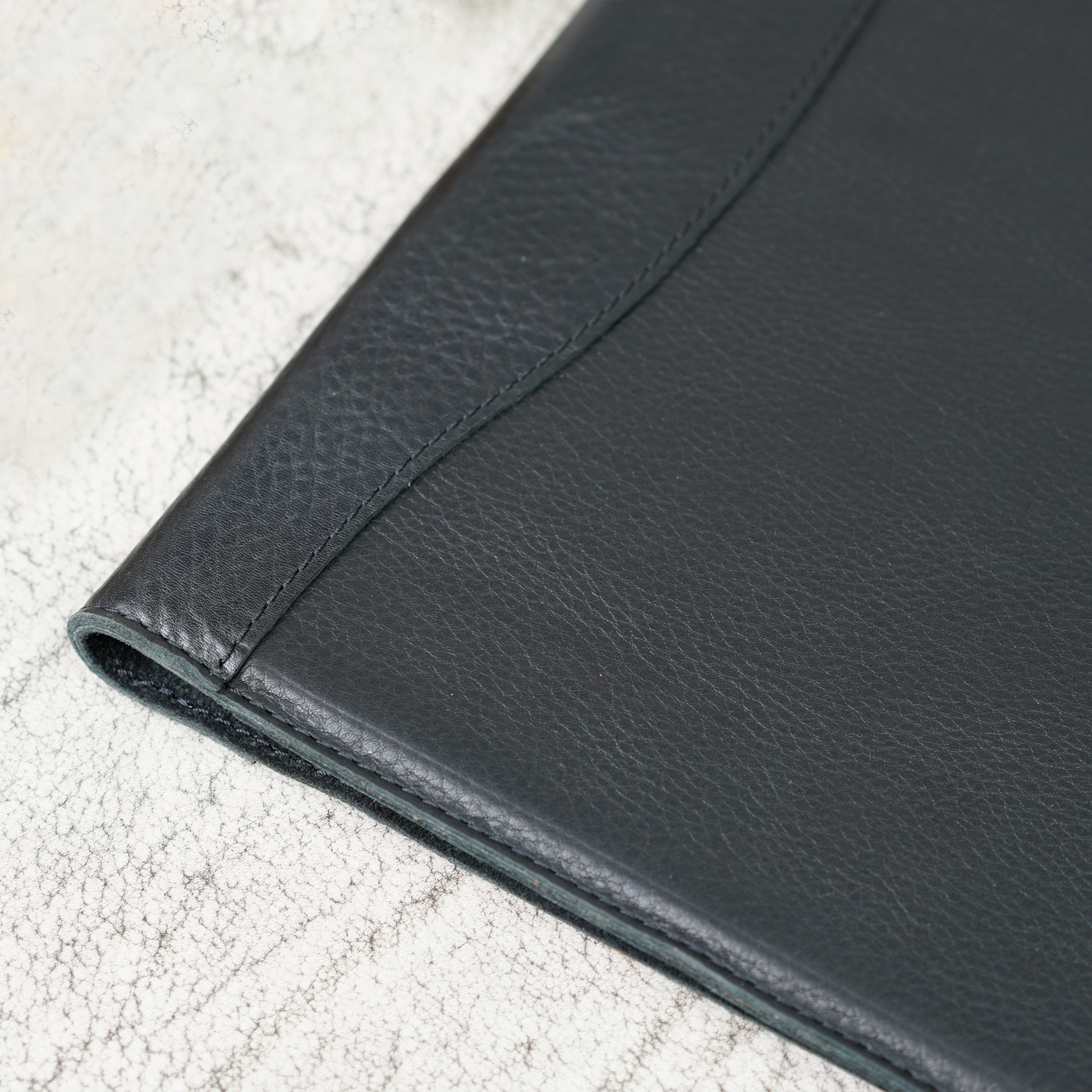 Close-up of the Marshall Padfolio in Dymnos Black, highlighting the rich texture and subtle grain of full-grain leather with tight, hand-stitched detail. A refined blend of craftsmanship and durability from Atelier PEGAI.