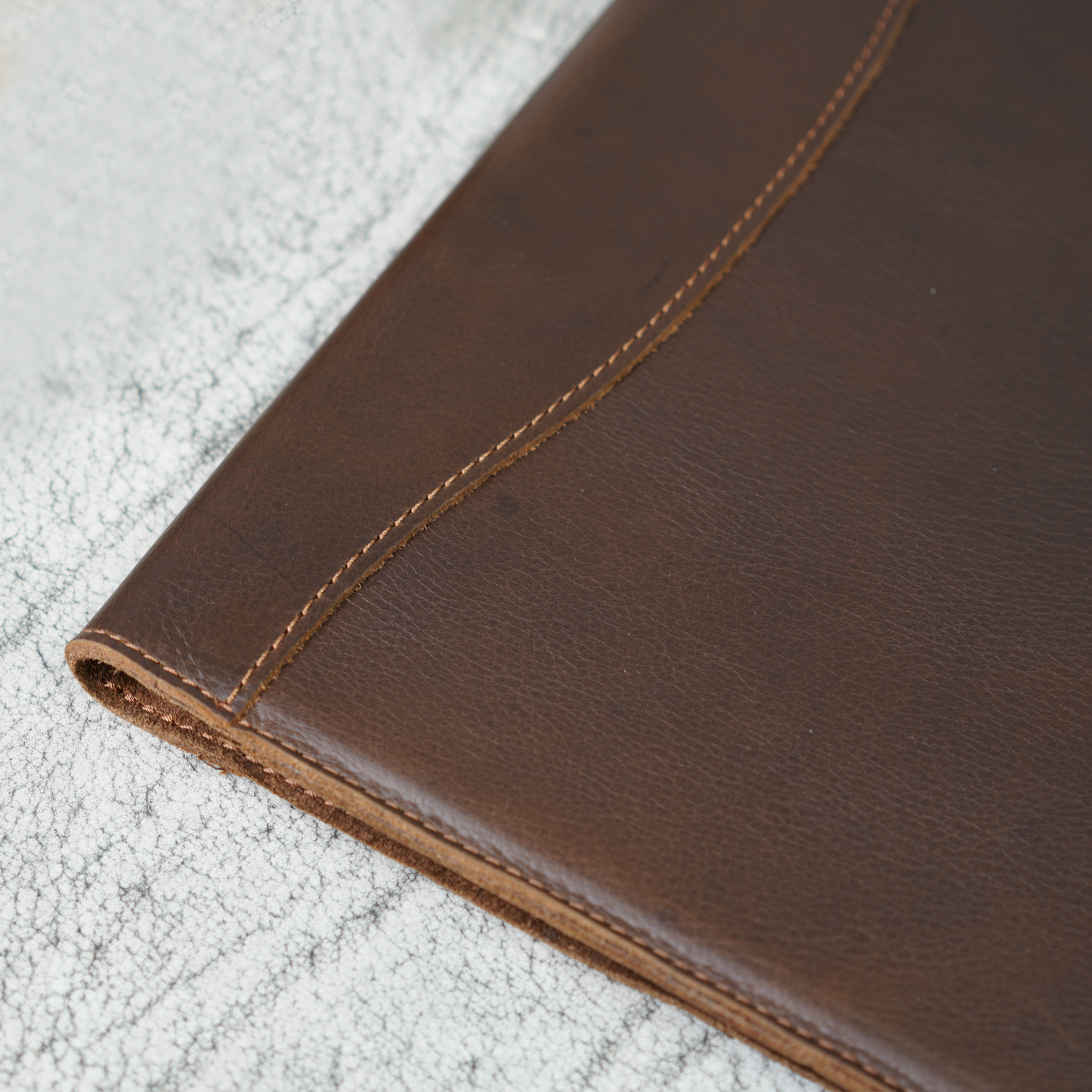 Close-up of the spine on the Marshall Padfolio in Dymnos Brown, showing rich leather texture, natural grain, and hand-stitched detailing. A quiet showcase of skilled craftsmanship and timeless durability.
