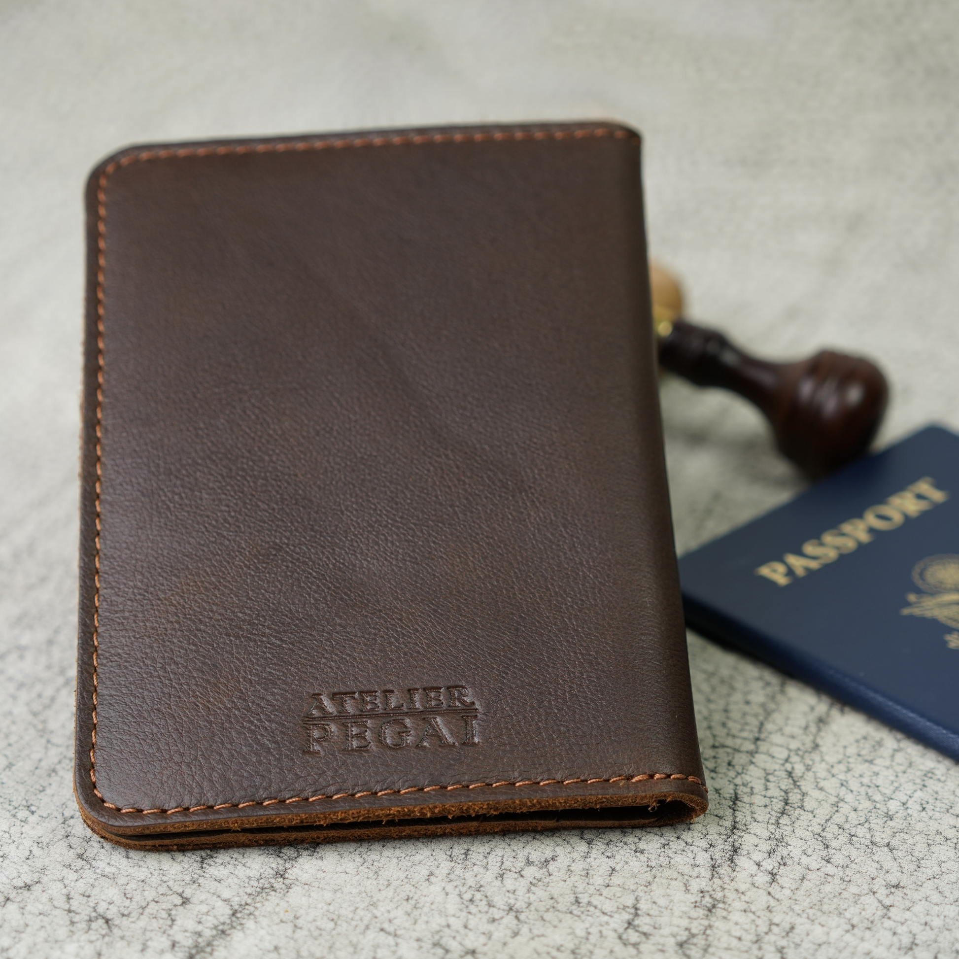 Close-up of the Dymnos Brown Pike Leather Passport Wallet by Atelier PEGAI, embossed with the brand’s signature mark. The supple leather and classic stitching invite you to carry something made with care—built for stories, not just storage.
