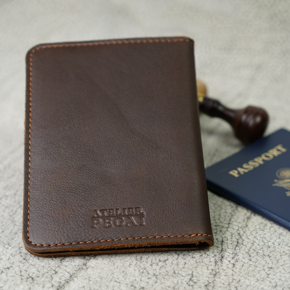 Close-up of the Dymnos Brown Pike Leather Passport Wallet by Atelier PEGAI, embossed with the brand’s signature mark. The supple leather and classic stitching invite you to carry something made with care—built for stories, not just storage.