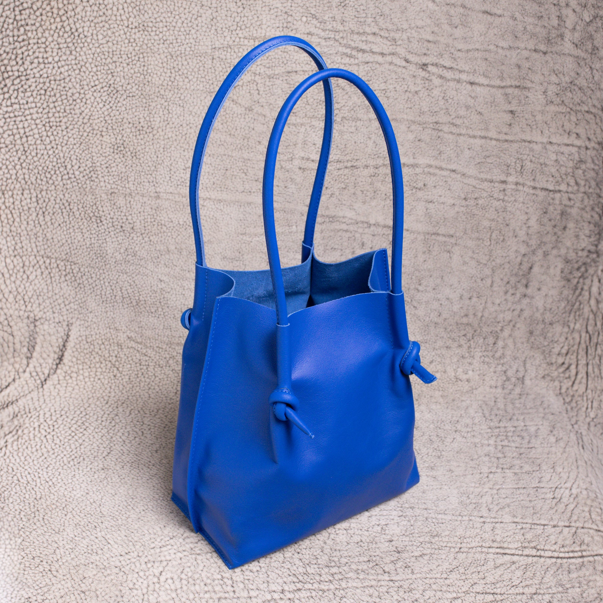 Three-quarter angled shot of the Flora Everyday Leather Tote in blue, highlighting its soft structure, dual handles, and spacious open-top design.