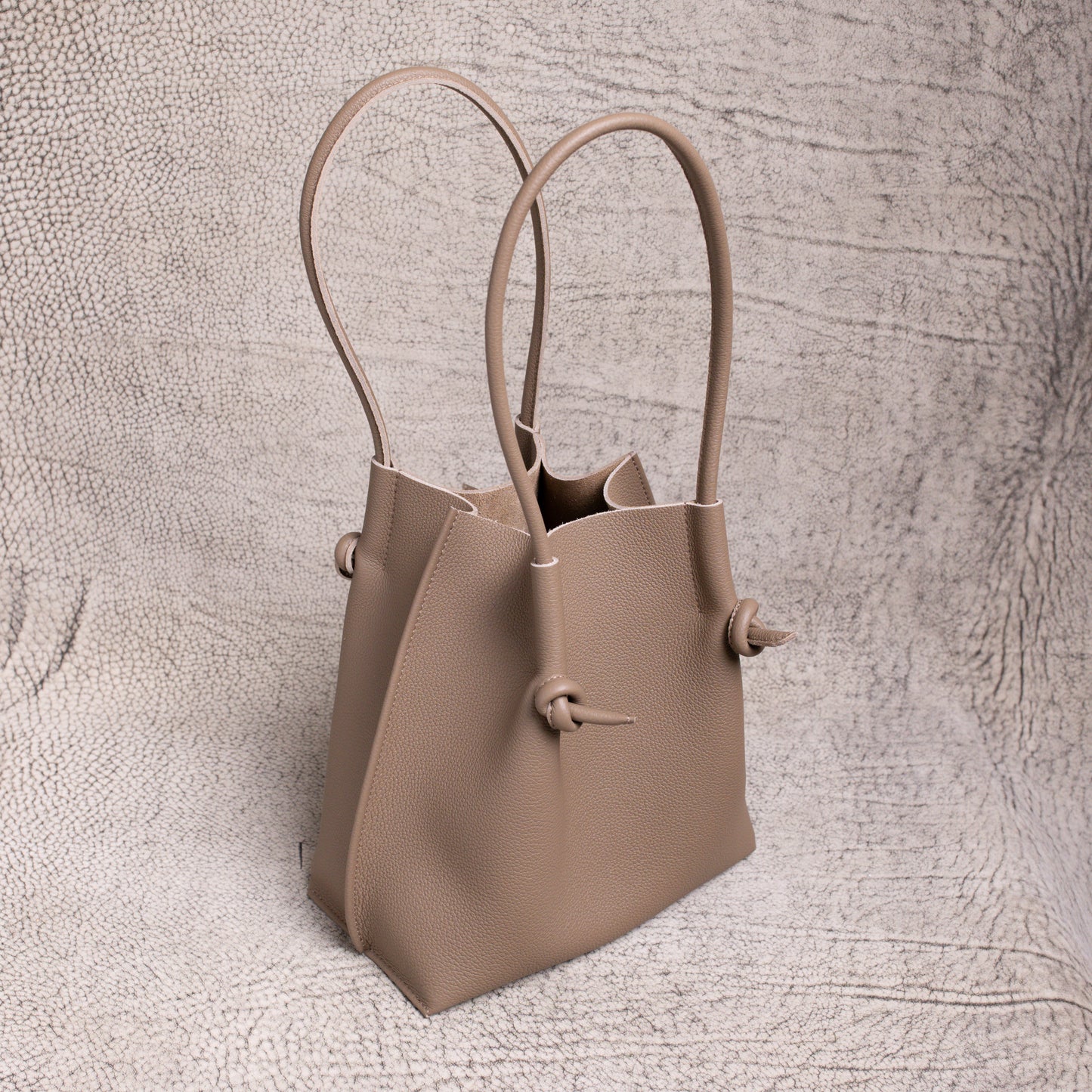 Angled shot of the Flora in Etoupe, highlighting the sculptural shape, upright handles, and folded-edge detailing.