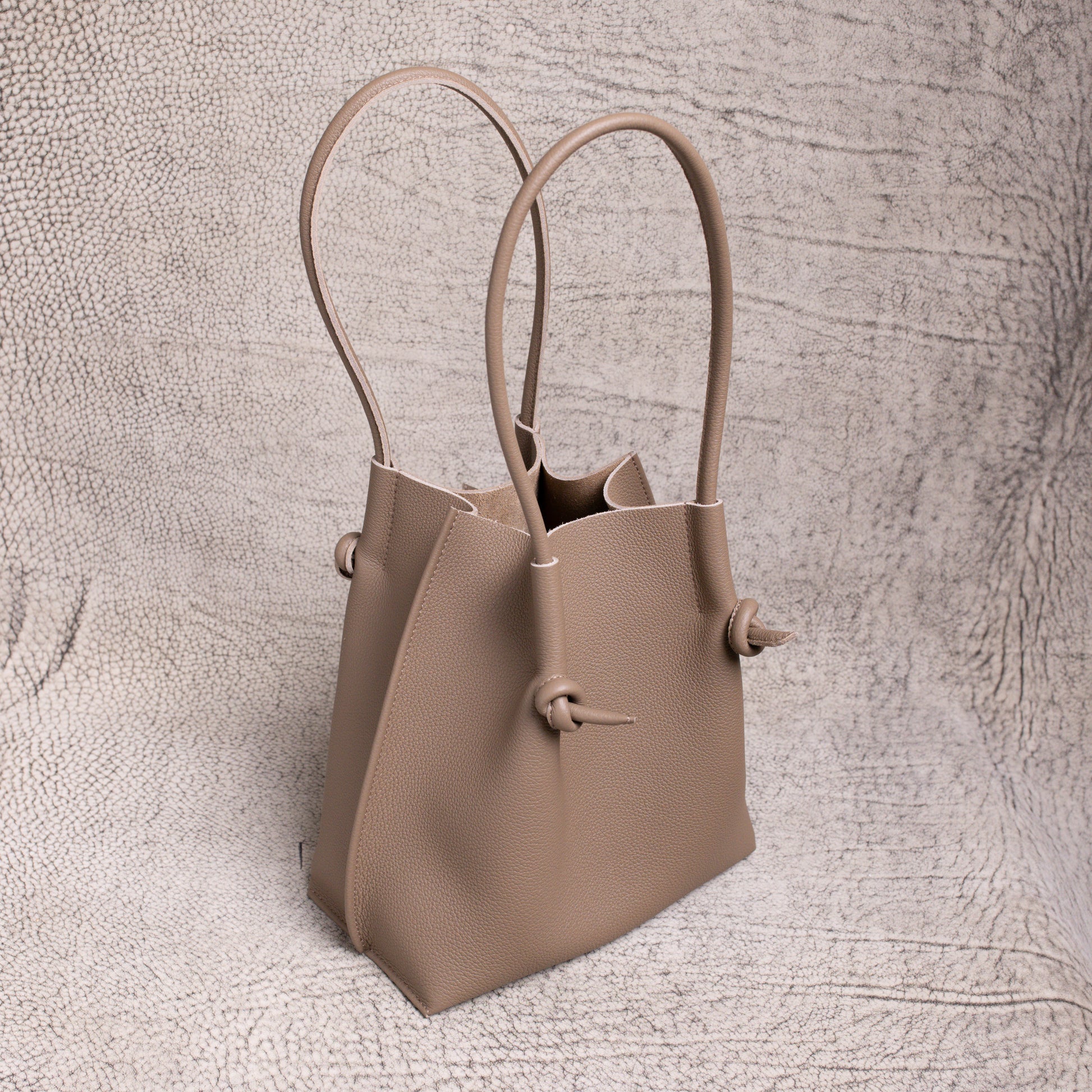 Angled shot of the Flora in Etoupe, highlighting the sculptural shape, upright handles, and folded-edge detailing.