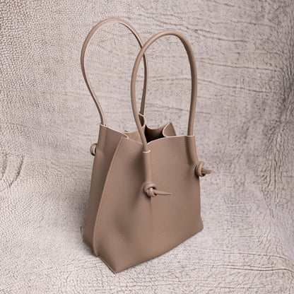 Angled shot of the Flora in Etoupe, highlighting the sculptural shape, upright handles, and folded-edge detailing.
