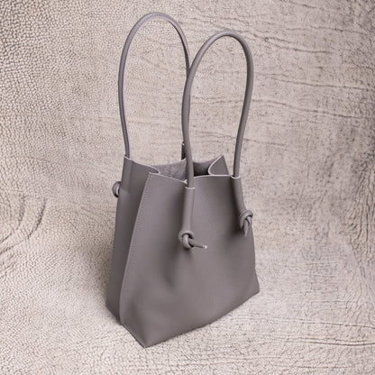 Three-quarter angle of the gray Flora tote, highlighting its sculpted silhouette and rolled handles against a neutral textured backdrop.