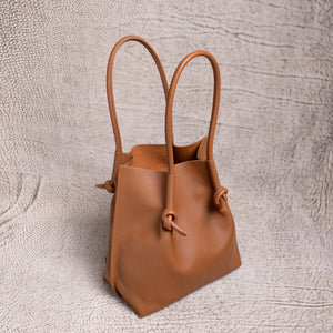 Angled view of the Flora Everyday Leather Tote in urban calf taba, featuring pebbled leather texture, raw suede interior, and knotted rolled handles.