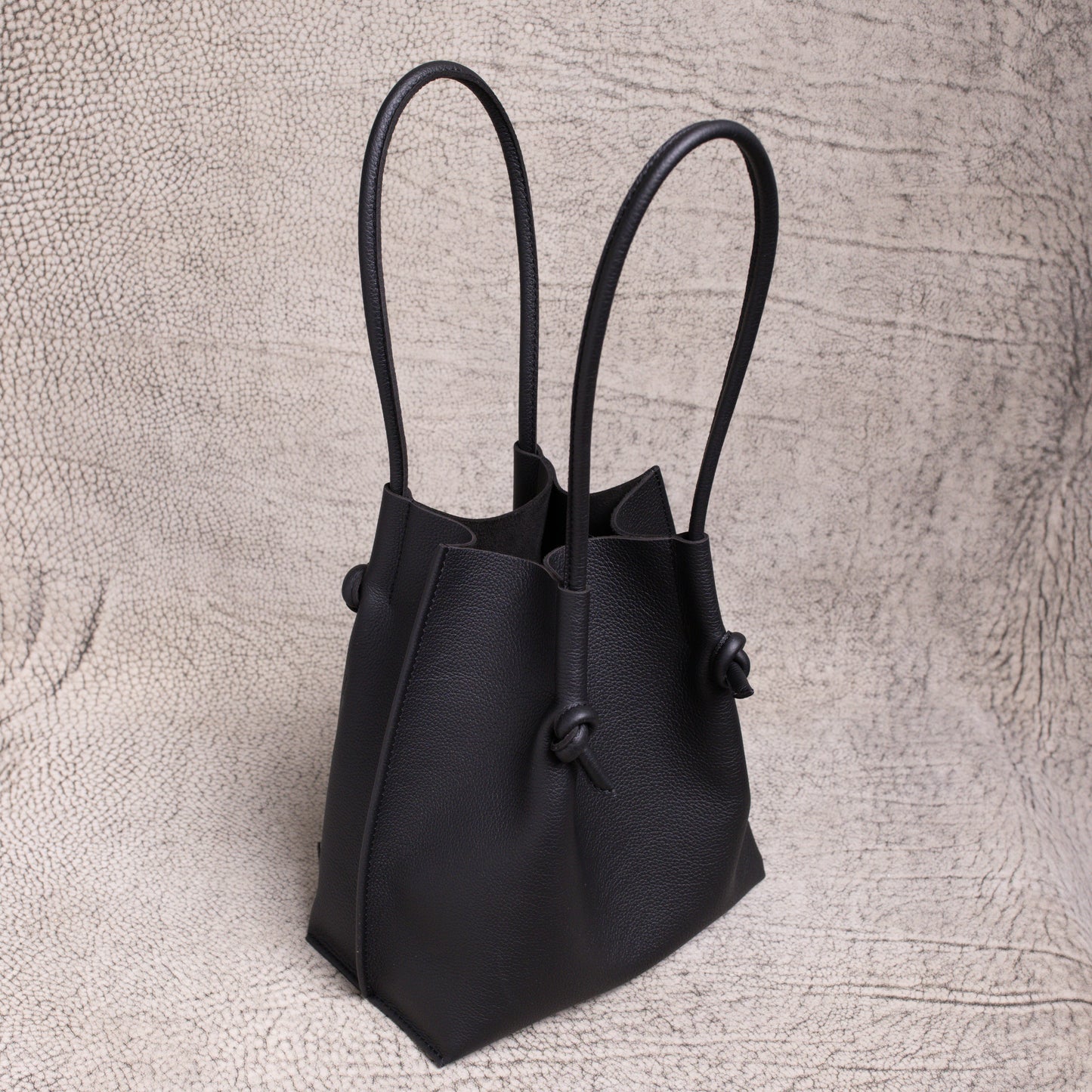 Three-quarter angle of the Flora tote revealing its elegant shape, dual rolled handles, and slouchy form in supple black calfskin.