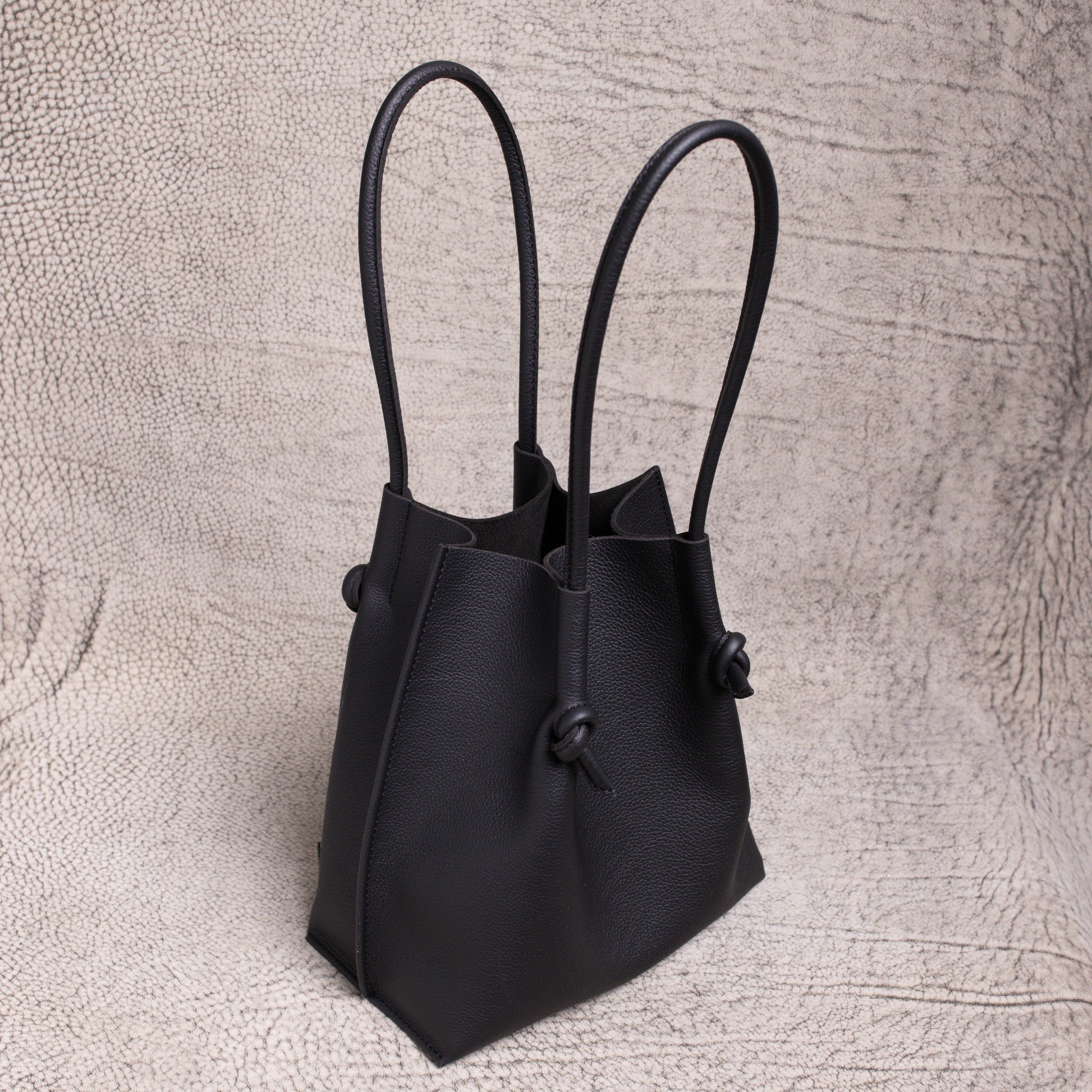 Three-quarter angle of the Flora tote revealing its elegant shape, dual rolled handles, and slouchy form in supple black calfskin.