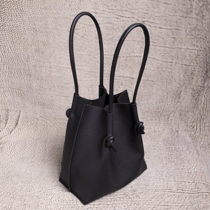 Three-quarter angle of the Flora tote revealing its elegant shape, dual rolled handles, and slouchy form in supple black calfskin.