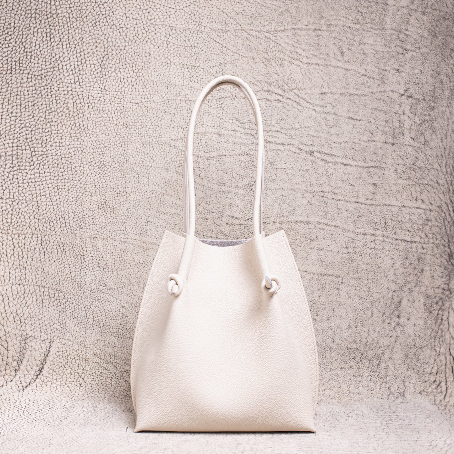 Flora Everyday Tote in Togo Beige leather standing upright on a textured surface.