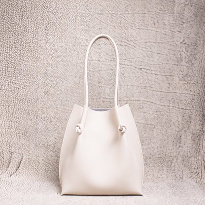 Flora Everyday Tote in Togo Beige leather standing upright on a textured surface.