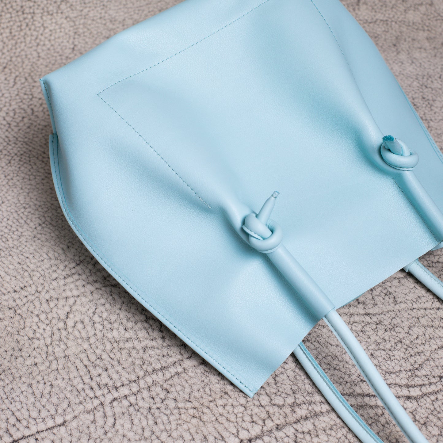 Close-up of the leather tote laid flat, highlighting the folded-edge construction and clean stitching along the base.