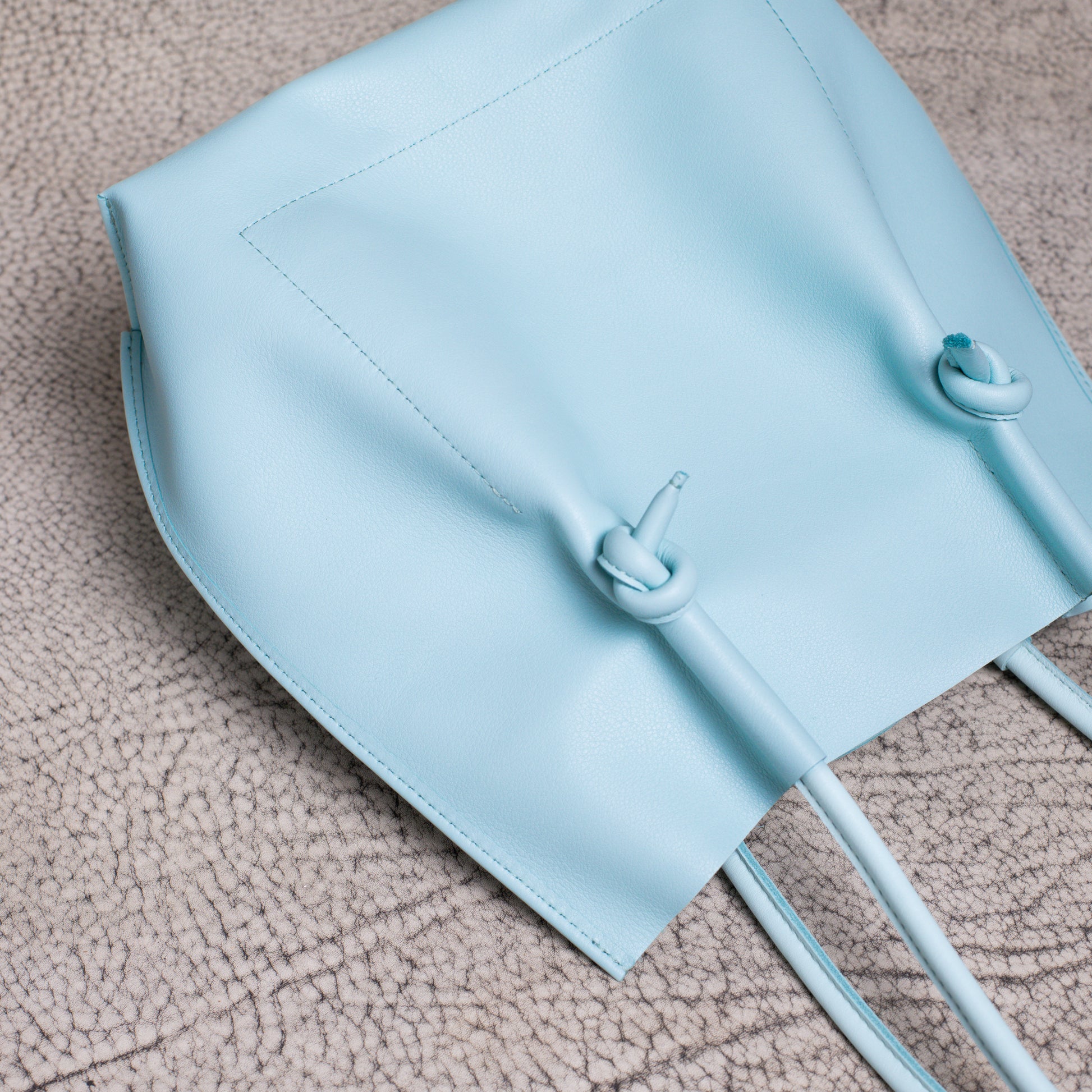 Close-up of the leather tote laid flat, highlighting the folded-edge construction and clean stitching along the base.