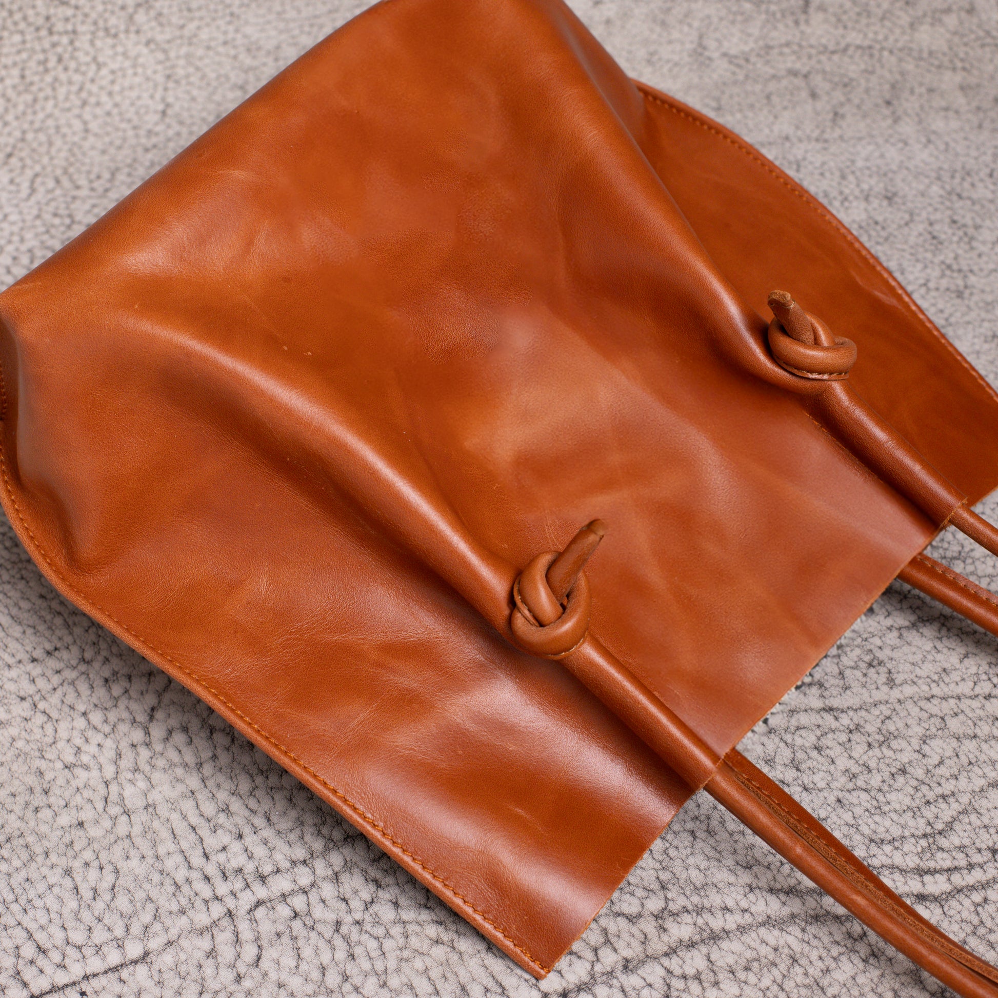 Close-up of the Flora tote laid flat, focusing on the smooth texture of the artisan leather and the unique knotted strap detailing.