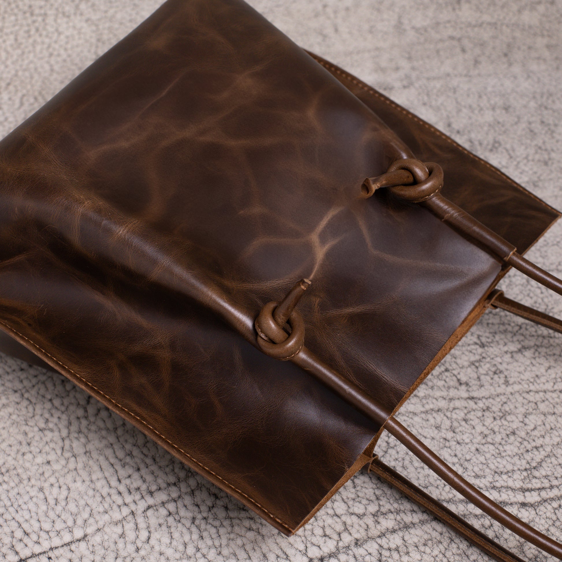 Close-up of the bottom knotted leather handles on the Flora Tote, highlighting the unique texture and hand-stitched craftsmanship.