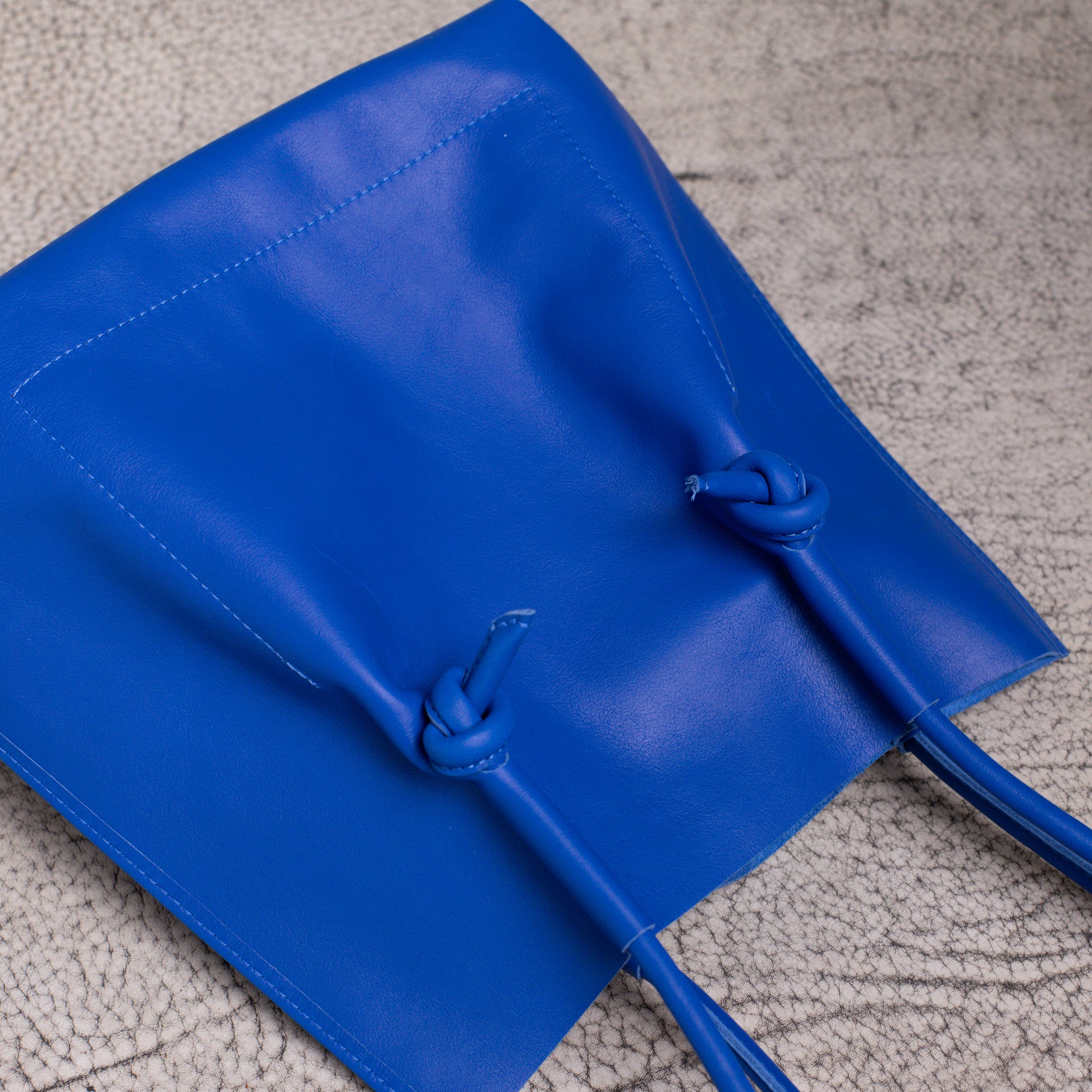 Close-up of the Flora tote lying flat, focusing on the craftsmanship of the knotted rolled handles and smooth calf leather texture.