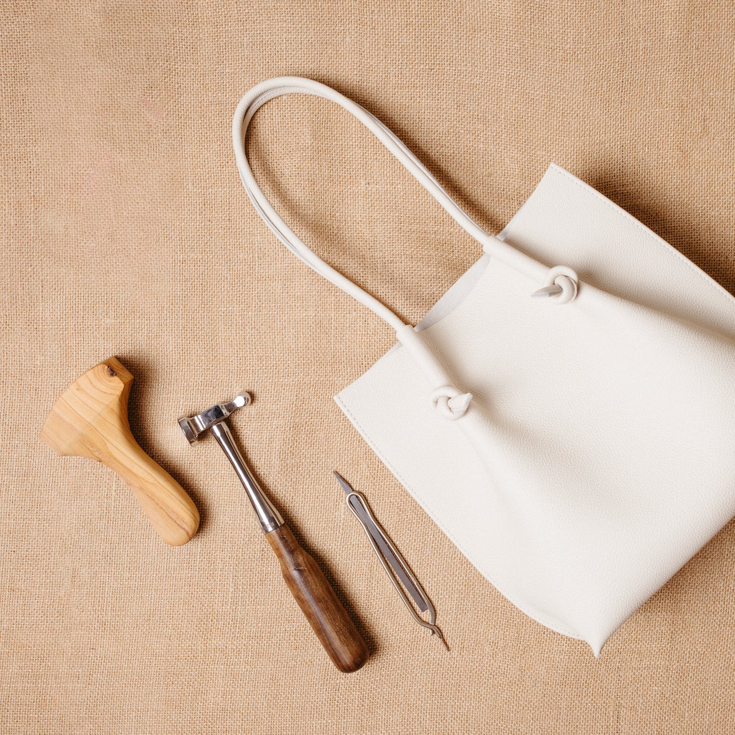 Beige Flora Tote laid beside leathercraft tools on burlap—evoking artisanal elegance.