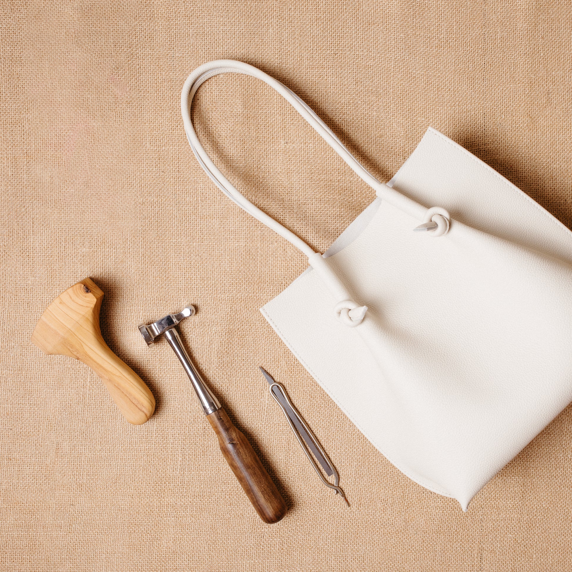 Beige Flora Tote laid beside leathercraft tools on burlap—evoking artisanal elegance.