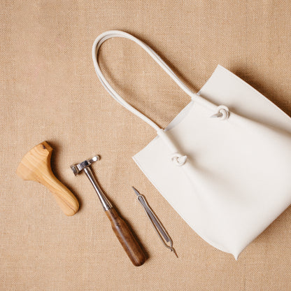 Beige Flora Tote laid beside leathercraft tools on burlap—evoking artisanal elegance.