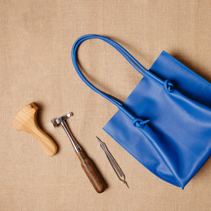 Flat lay of the Flora Leather Tote in blue next to artisan tools, emphasizing its handcrafted quality and Atelier PEGAI’s dedication to traditional leatherwork.