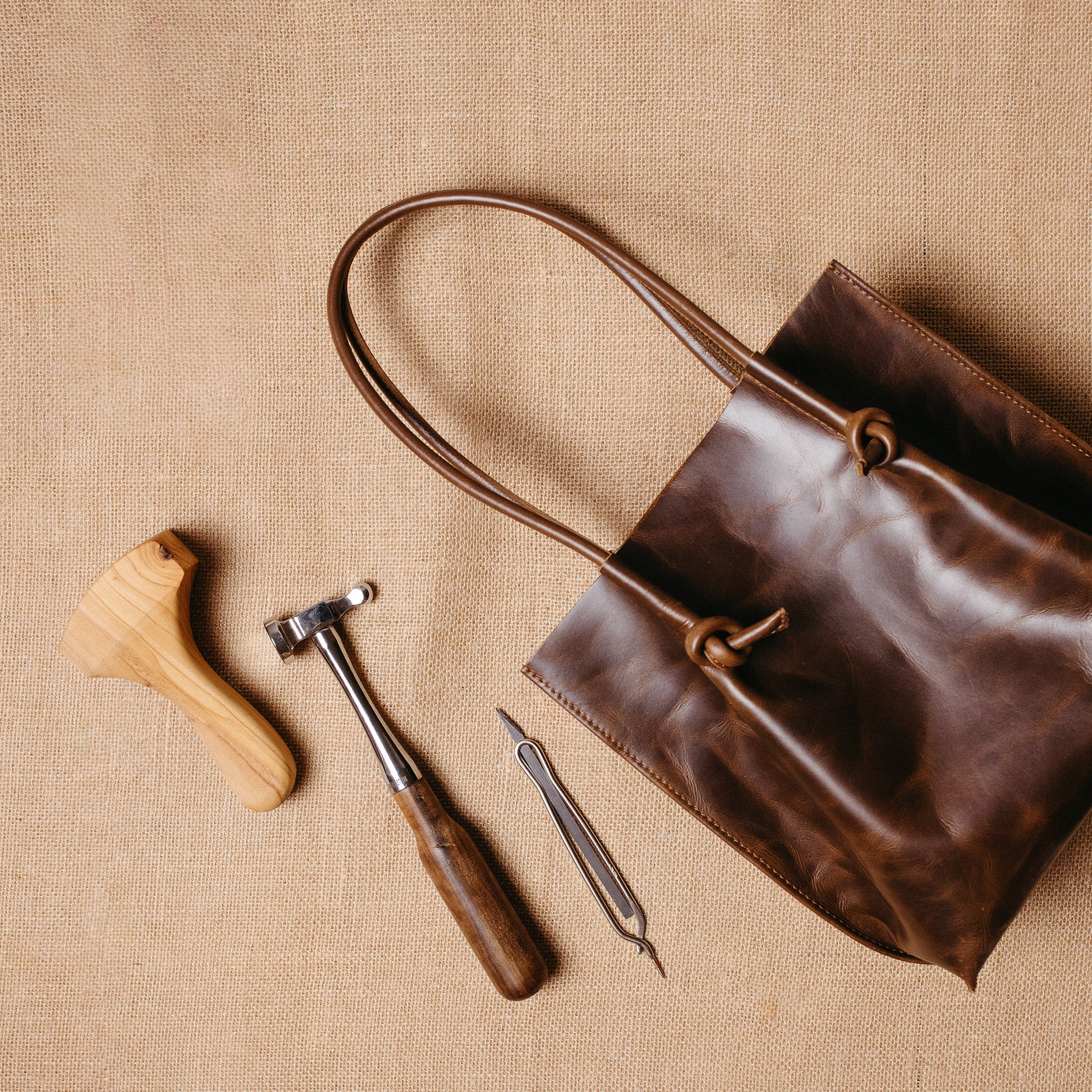 The Flora Everyday Tote laid flat with leatherworking tools beside it, reflecting Atelier PEGAI’s handcrafted roots and raw suede interior.