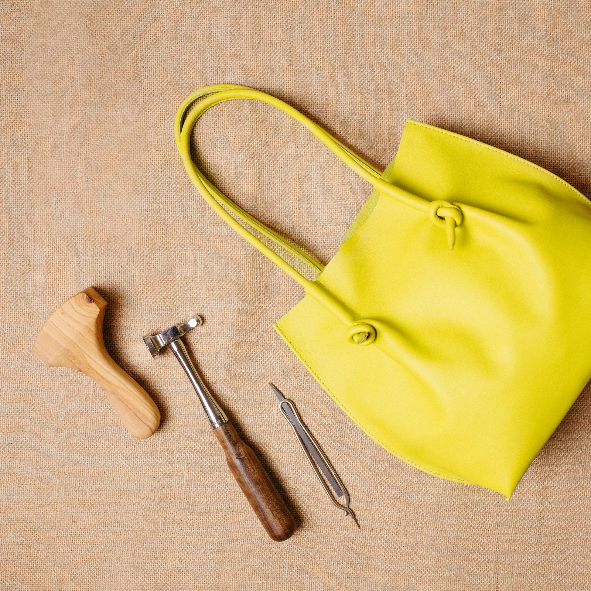 The Flora Everyday Tote laid flat beside traditional leatherworking tools, illustrating its handmade craftsmanship in Spain.