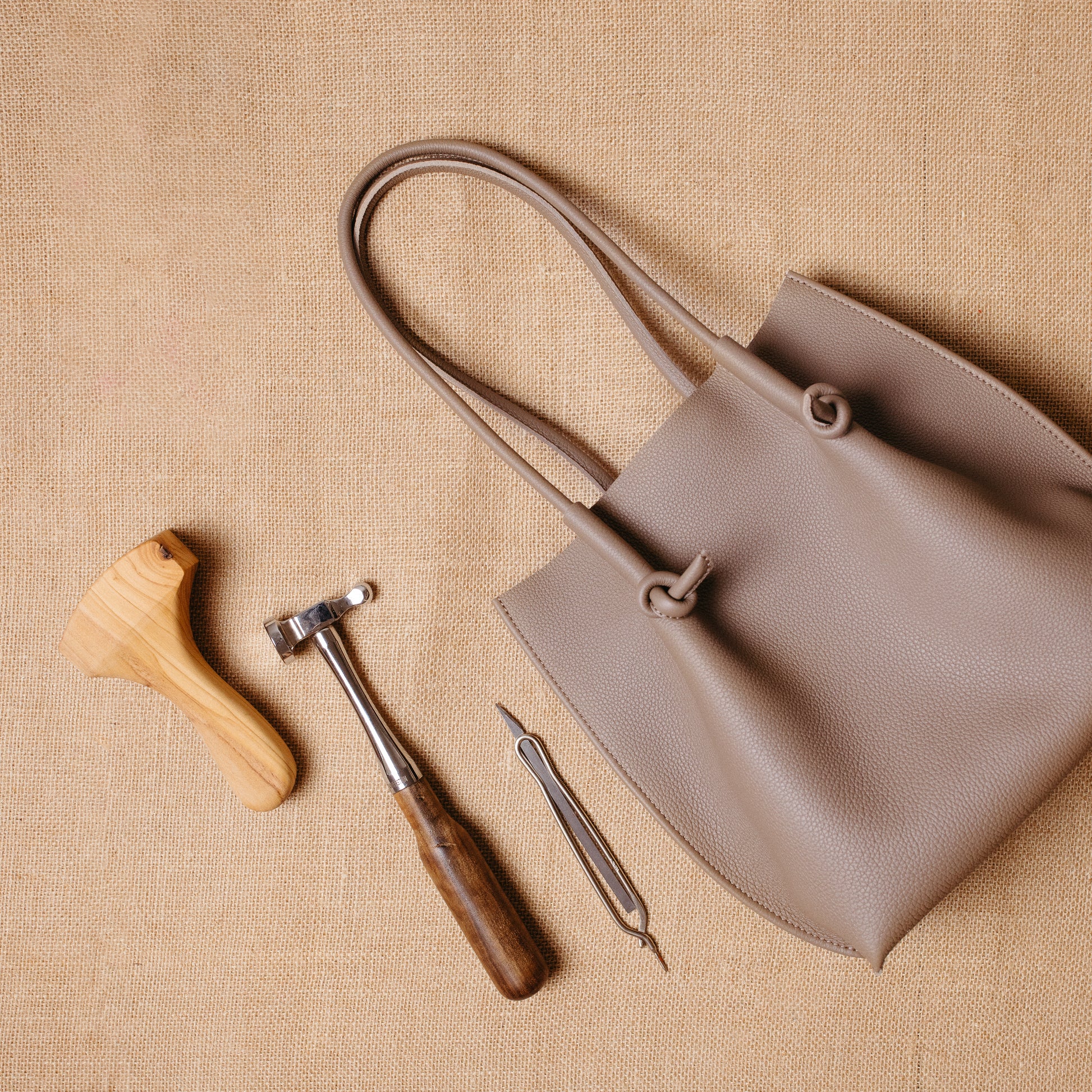 Flat lay of the tote beside leatherworking tools, connecting the finished product to its artisanal craftsmanship.