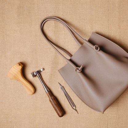 Flat lay of the tote beside leatherworking tools, connecting the finished product to its artisanal craftsmanship.