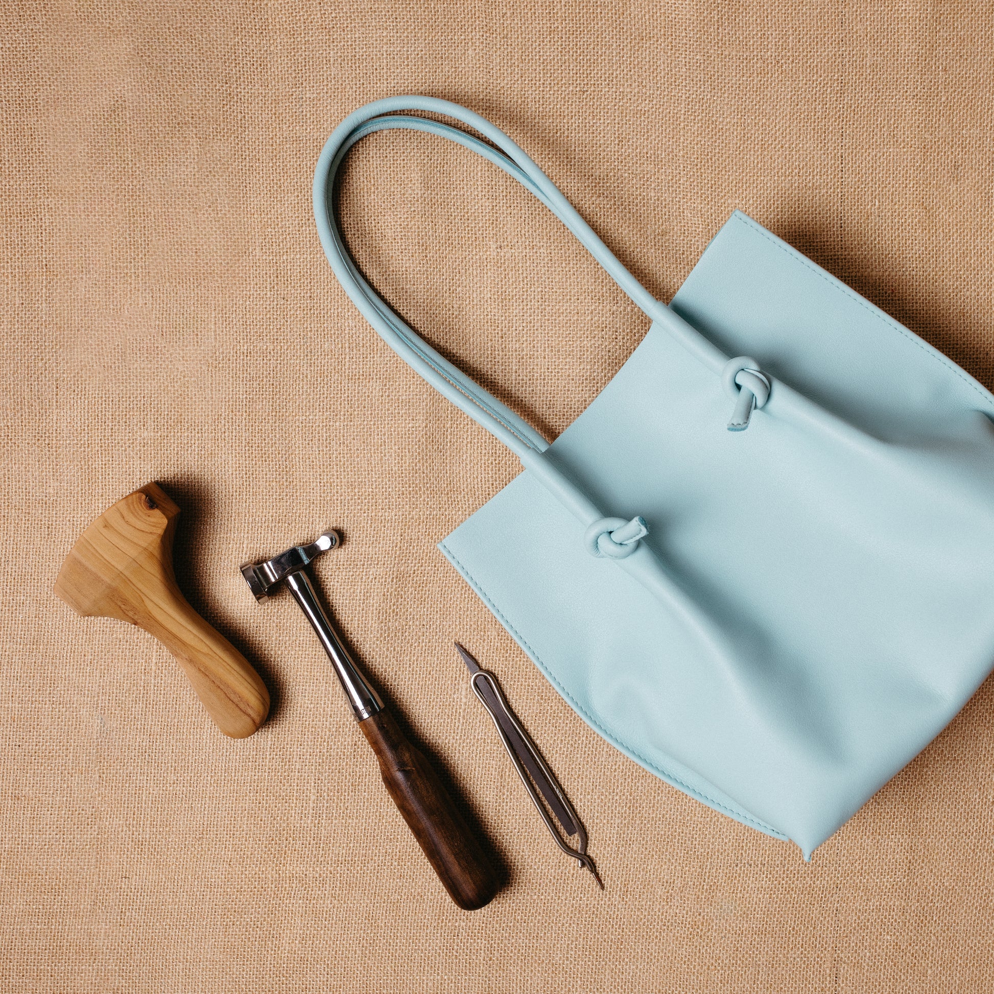 The Flora leather tote beside artisanal leatherworking tools, representing handcrafted design and fine Spanish craftsmanship.