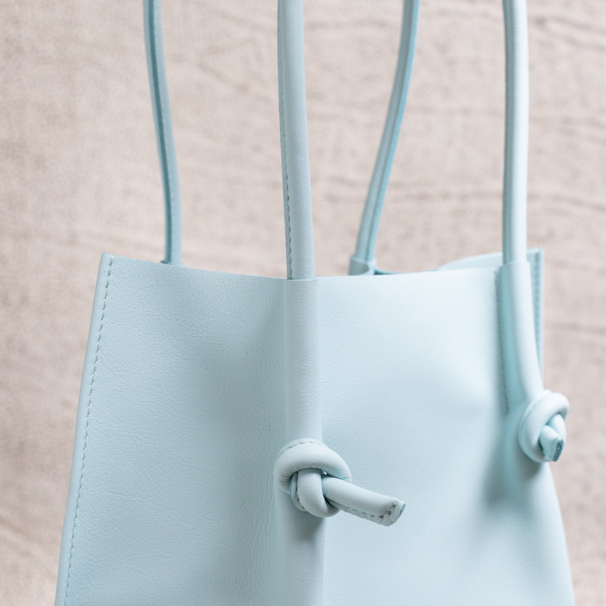 Detail view of the tote’s smooth rolled handle and knotted accent, showcasing the supple leather texture and precise stitching.