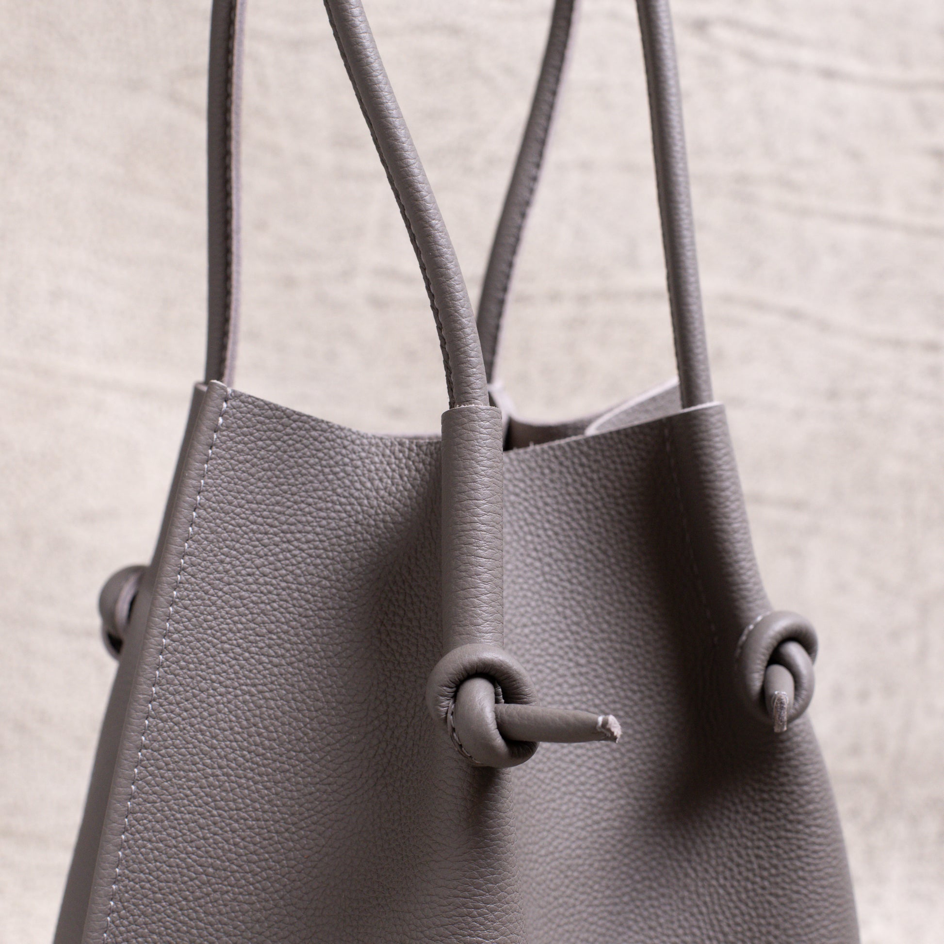 Side angle shot focusing on the dual handles and the tote’s signature knotted construction in gray calfskin.