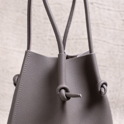 Side angle shot focusing on the dual handles and the tote’s signature knotted construction in gray calfskin.