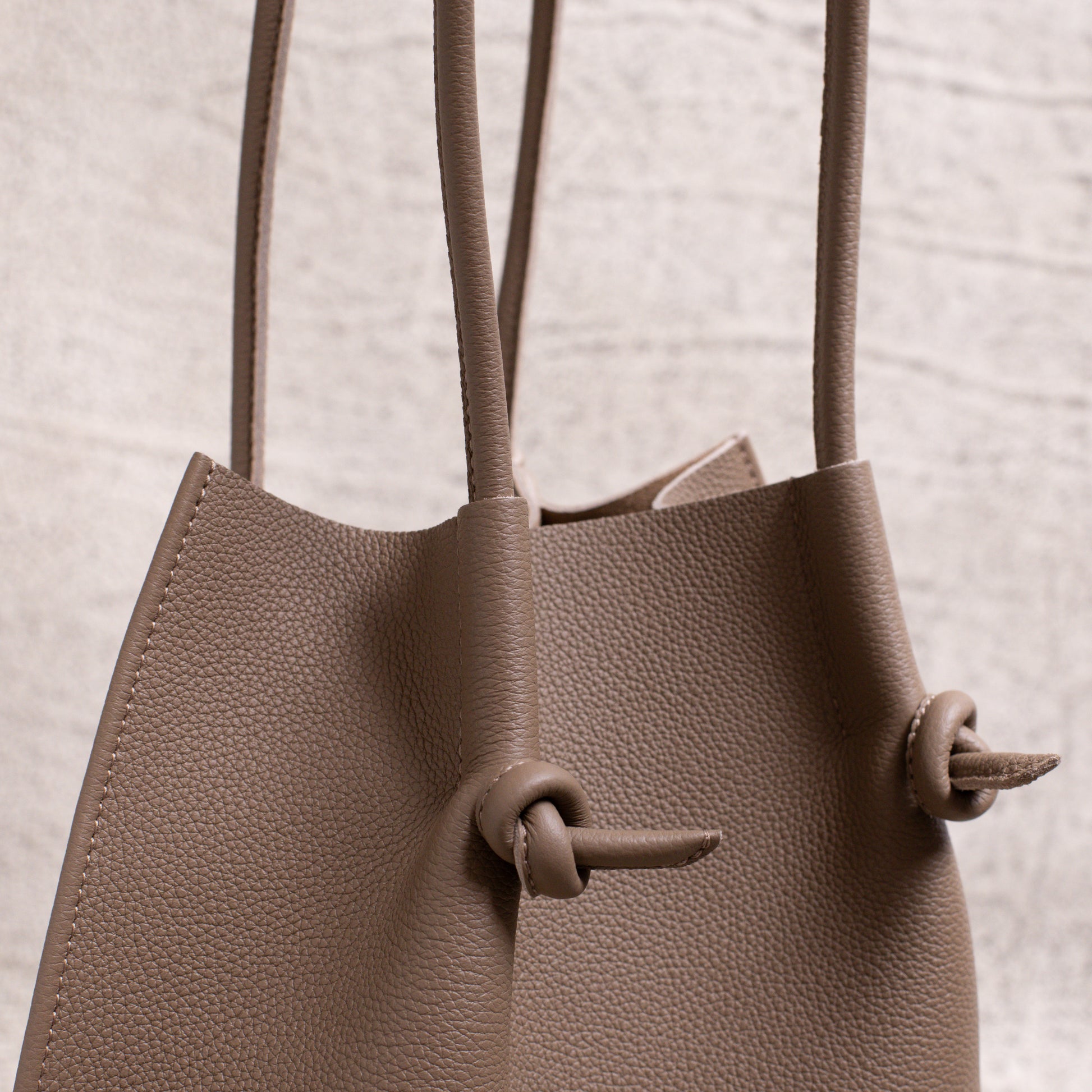 Side detail close-up showing the folded seam, dual handles, and signature knotted leather accents of the Etoupe edition.