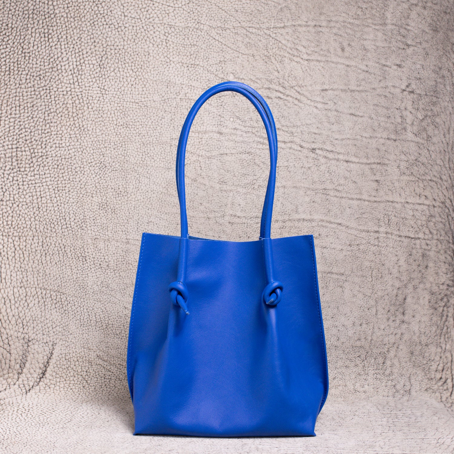 Front view of the Flora Everyday Leather Tote in Smooth Calf Blue, showcasing its minimalist silhouette and knotted leather handles.