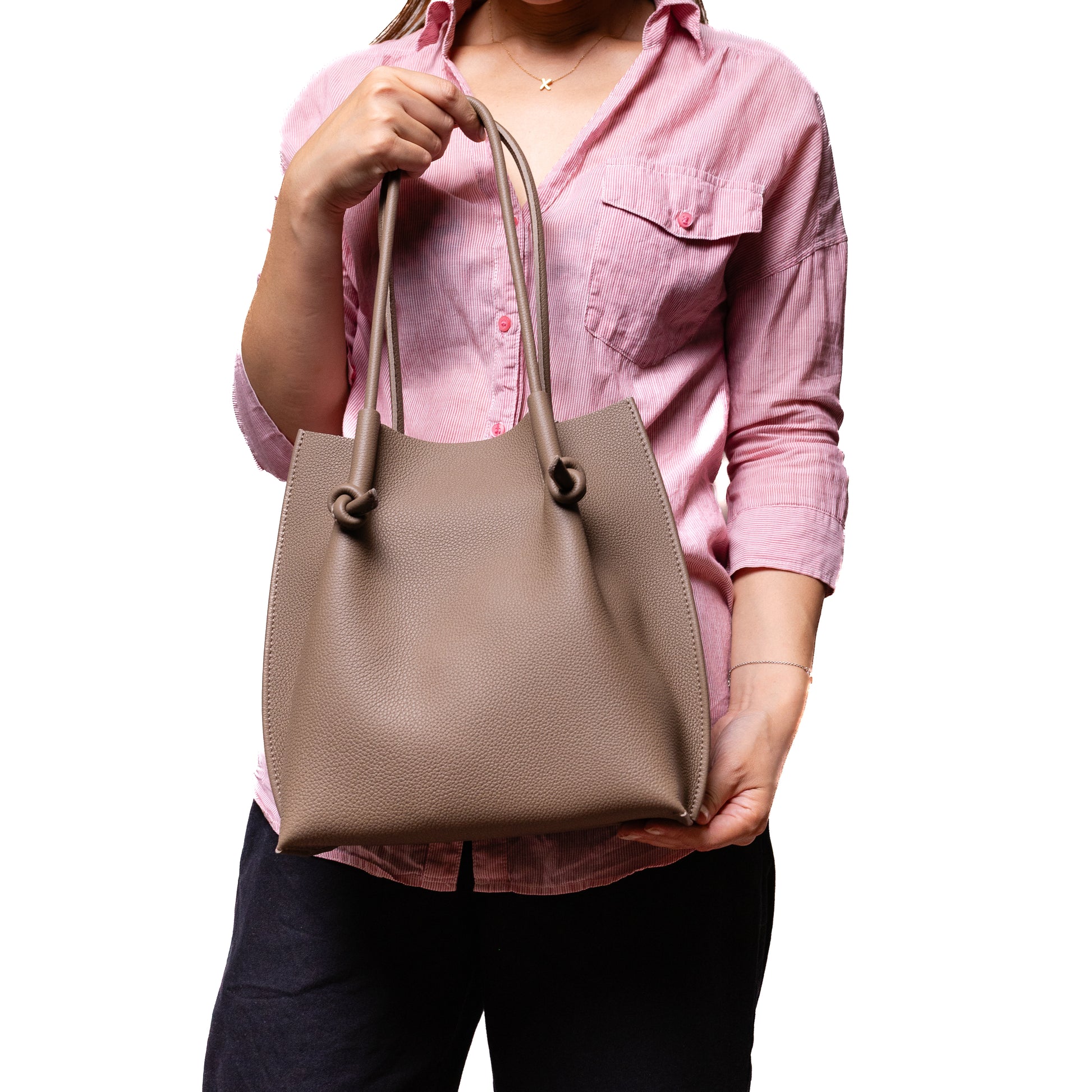 Model in a pink shirt holding the Flora Tote in Etoupe, offering a real-world sense of scale and styling ease.
