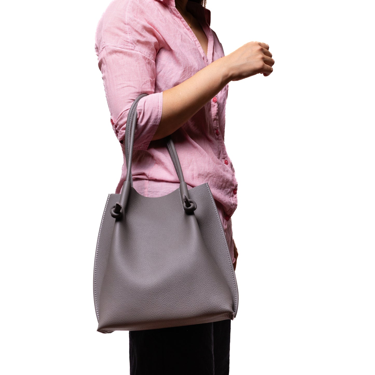 Model wearing a pink blouse carries the Flora Everyday Tote in gray, showing its size and elegant shape in a lifestyle setting.
