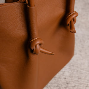 Macro view of the Flora tote’s signature knotted handle in tan leather, capturing the smooth finish and craftsmanship in the hand-tied detail.
