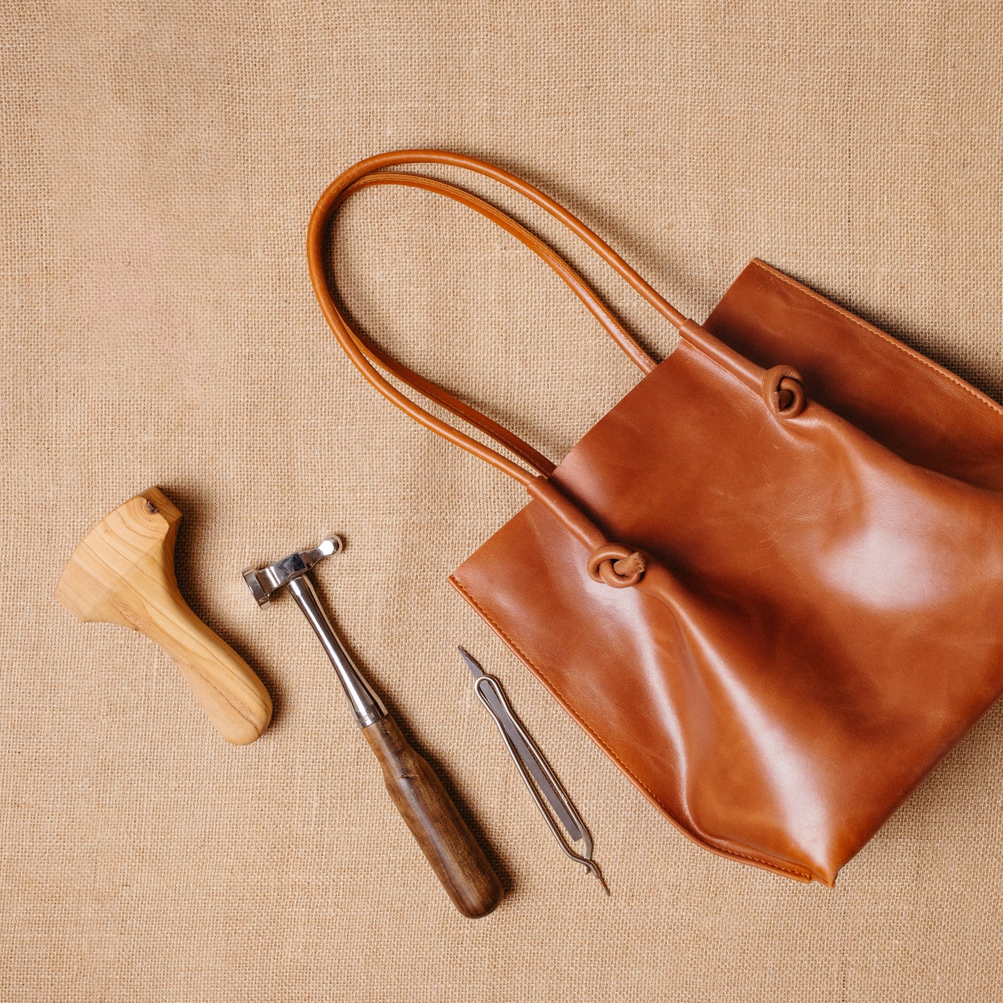 Top-down view of the Flora tote next to leathercraft tools, evoking the artisanal process behind its handmade construction in Spain.