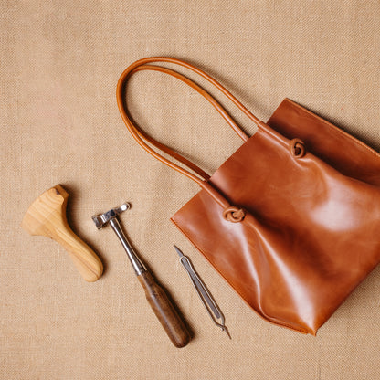 Top-down view of the Flora tote next to leathercraft tools, evoking the artisanal process behind its handmade construction in Spain.